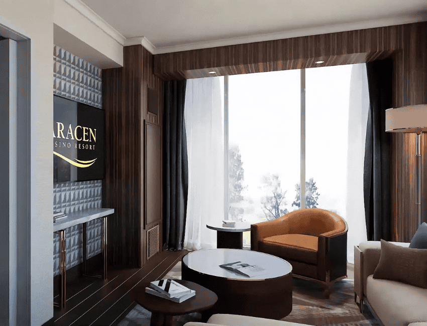 Modern hotel room lounge with a wall-mounted TV, round tables, armchairs, large window with sheer curtains, and wood-paneled walls.
