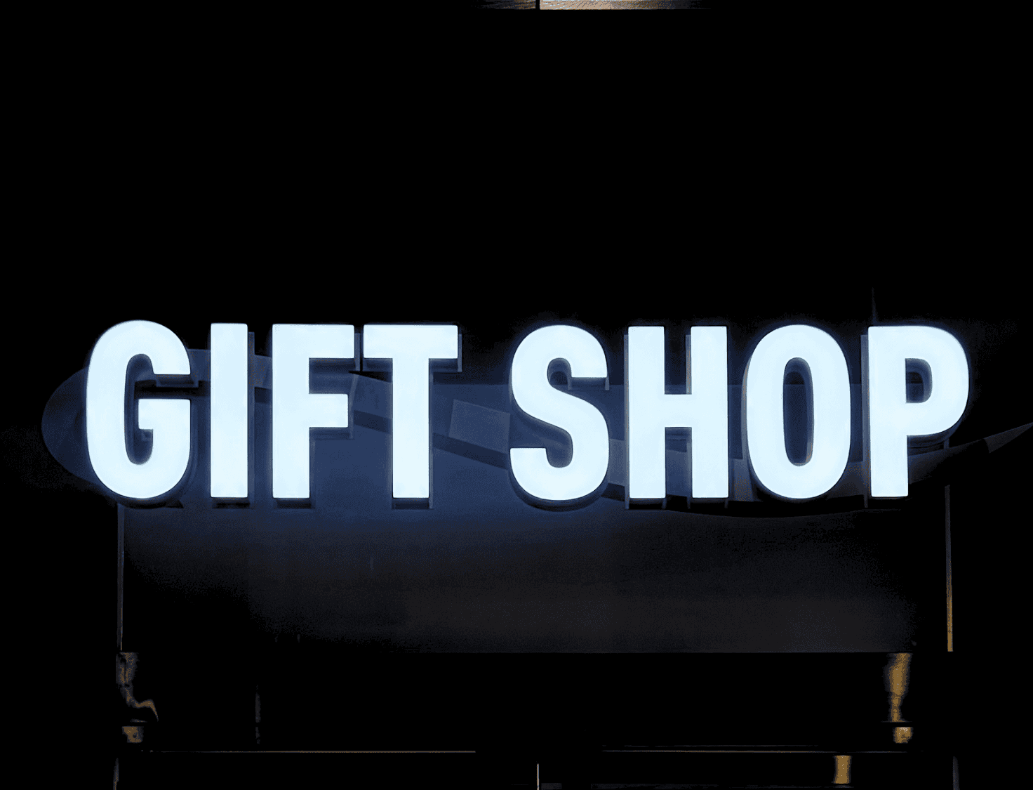 Illuminated “GIFT SHOP” sign against a dark background.